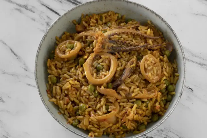 Un delicioso plato de arroz con calamares y guisantes, servido en un cuenco sobre una superficie de mármol.