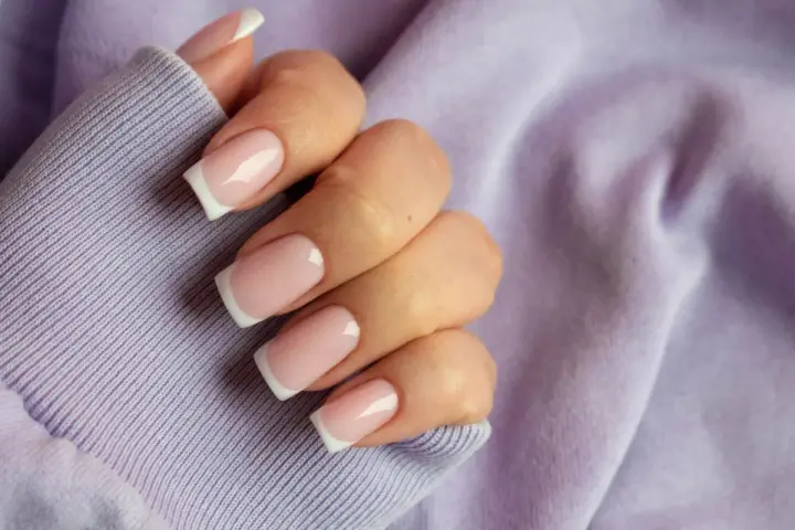 Dłoń z paznokciami w stylu french kolor, na tle lawendowej bluzy. Klasyka i elegancja.