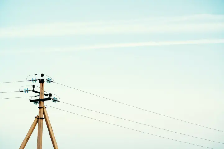 Drewniany słup na działce, który stoi tam od ponad 30 lat, z przewodami elektrycznymi na tle jasnego nieba.