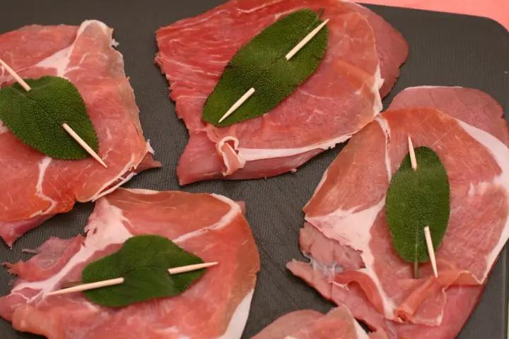 Fette di vitello pronte per la saltimbocca alla romana ricetta originale, con prosciutto crudo e foglie di salvia fissate con stuzzicadenti.
