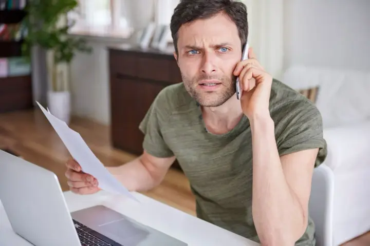 Zmartwiony mężczyzna z dokumentami w ręku rozmawia przez telefon, martwiąc się o niespłacony kredyt odnawialny.