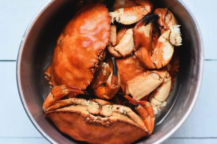 Un cuenco metálico lleno de buey de mar cocido, con sus caparazones anaranjados y pinzas visibles.