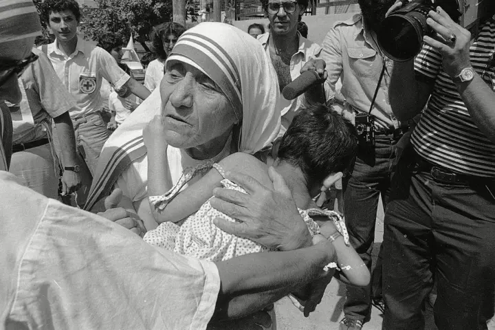 Missionaries of Charity founder, Mother Teresa, cradles a child amidst a crowd and media attention.