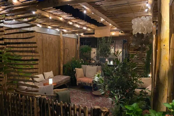 Une terrasse de jardin aménagée en coin cocooning, avec des banquettes confortables, des lumières douces et une ambiance chaleureuse.