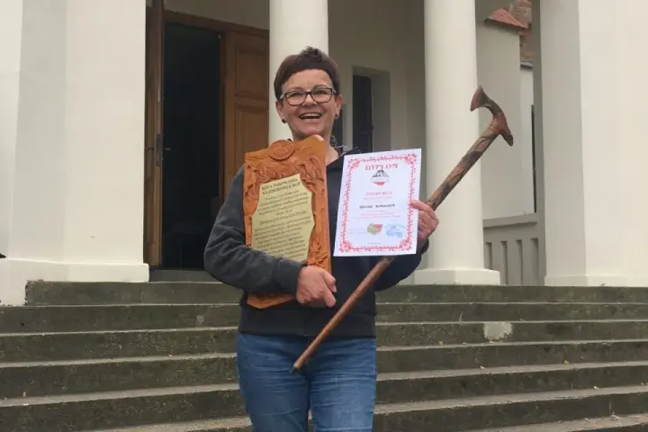 Uśmiechnięta kobieta z dyplomem i drewnianą laską, zdobywczyni Korony Gór Polskich.