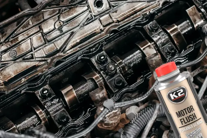 Silnik Peugeot 307 1.6 benzyna po płukaniu. Widać wałki rozrządu i elementy pokryte olejem. Obok butelka płukanki K2 Motor Flush.
