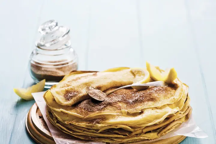 Pile de crêpes au lait entier, saupoudrées de sucre et de cannelle, garnies de quartiers de citron. Un délice simple et gourmand.
