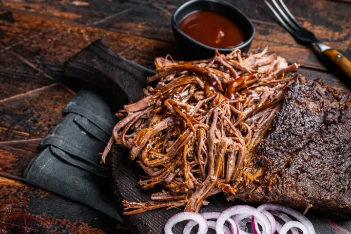 Soczysta, aromatyczna szarpana wołowina, polana sosem BBQ, podana z krążkami cebuli na drewnianej desce. Idealna na grilla.