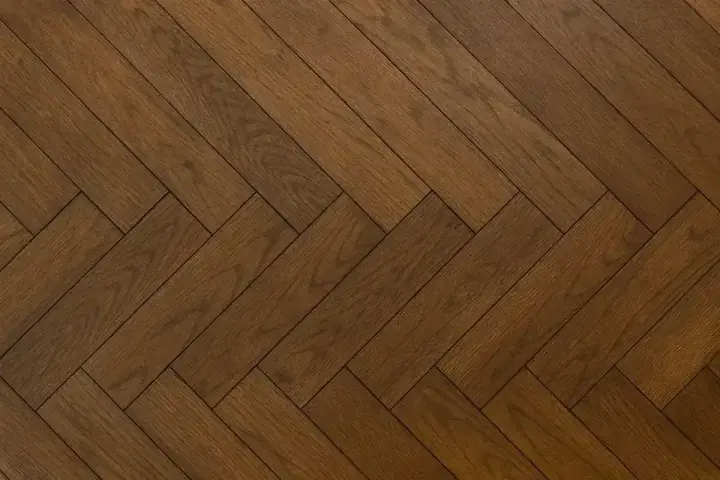 Vacker fiskbensparkett i mörkt trä, redo att slipa för att återfå sin glans.