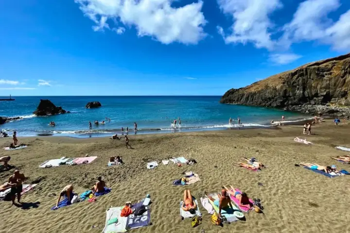 Słoneczne madera plaże z turystami kąpiącymi się w turkusowym oceanie i opalającymi się na piasku.