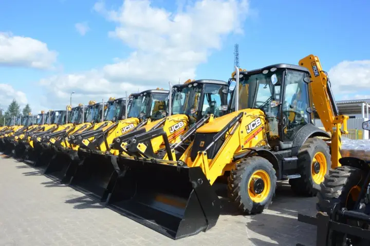 Rząd żółtych koparko-ładowarek JCB stoi na placu.