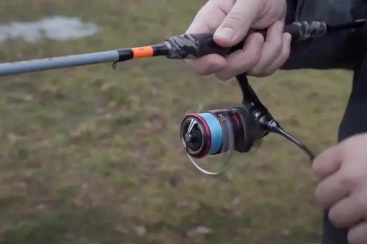 Daiwa Fuego Camo Spin Test: Eine Hand hält eine Angelrute mit Camo-Griff und einer Rolle mit blauer Schnur.