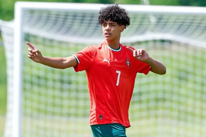 Cristiano Ronaldo Jr. con pelo rizado y camiseta roja con el número 7, señalando con el dedo índice.