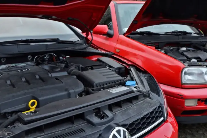 Dwa czerwone Volkswageny z otwartymi maskami. Nowszy model z silnikiem TDI obok starszego, gdzie widać stary diesel.