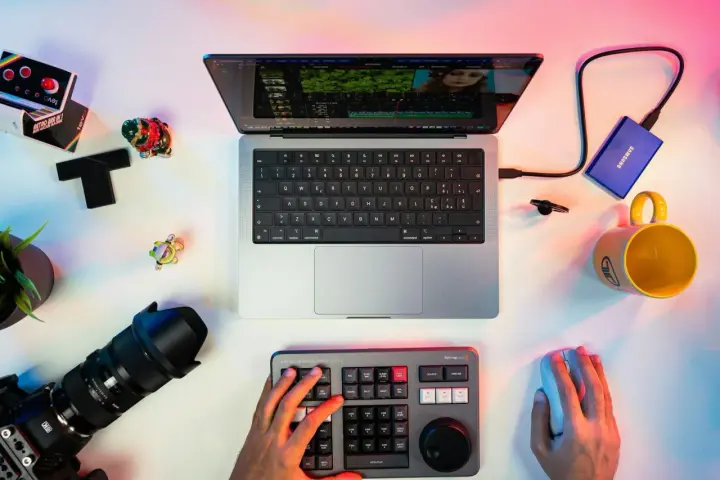 Un escritorio con un portátil mostrando un editor de video, un teclado de control, cámara, disco duro y taza. Ideal para los mejores editores de video para PC.