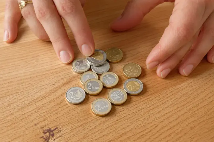 Mains disposant des pièces de 2 euros bremen 2010 sur une table en bois.