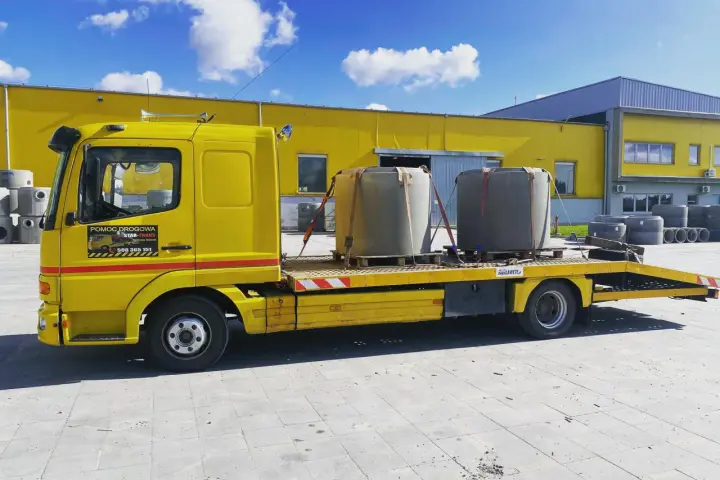 Żółta laweta z dwoma betonowymi elementami, gotowa do transportu. To **assistance warta** uwagi, gdy potrzebujesz przewieźć ciężkie ładunki.