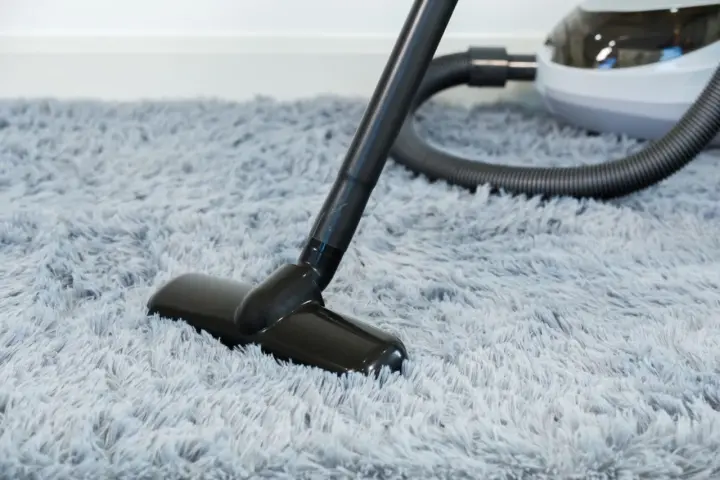Vacuum cleaner head on a fluffy grey rug, demonstrating how to wash a rug by removing dust and debris.