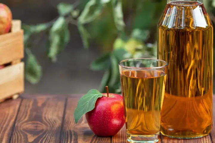 Manzana roja junto a un vaso y botella de vinagre de manzana para limpiar. Cosecha fresca en caja de madera al fondo.