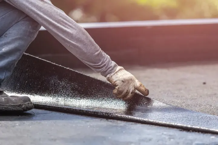 Hand mit Handschuh legt neue Dachpappe an. Alte Dachpappe entsorgen ist der nächste Schritt.