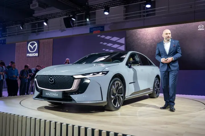 Elegancki, szary sedan Mazda6e prezentowany na scenie przez mężczyznę w garniturze.