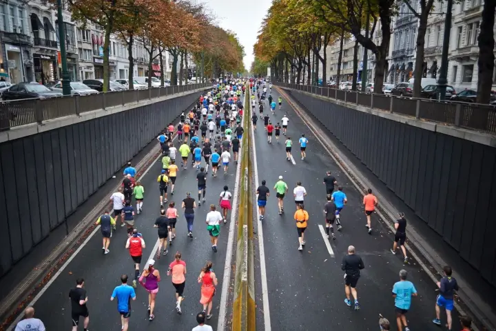 Stor grupp löpare i en stadsgata, många deltagare som springer maraton.