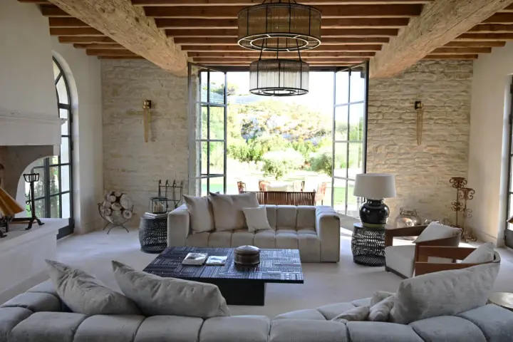 L'intérieur d'un mas provençal baigné de lumière, avec des poutres apparentes, des murs en pierre et une vue imprenable sur la campagne.