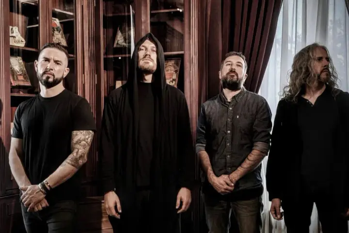 Quatre musiciens, dont un avec une capuche, posent devant des étagères remplies de livres. Ce groupe metal français connu dégage une aura mystérieuse.