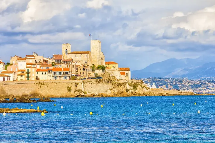 Vista de la ciudad amurallada de Antibes, Francia, con sus torres y edificios coloridos sobre un acantilado, bañada por el mar azul.
