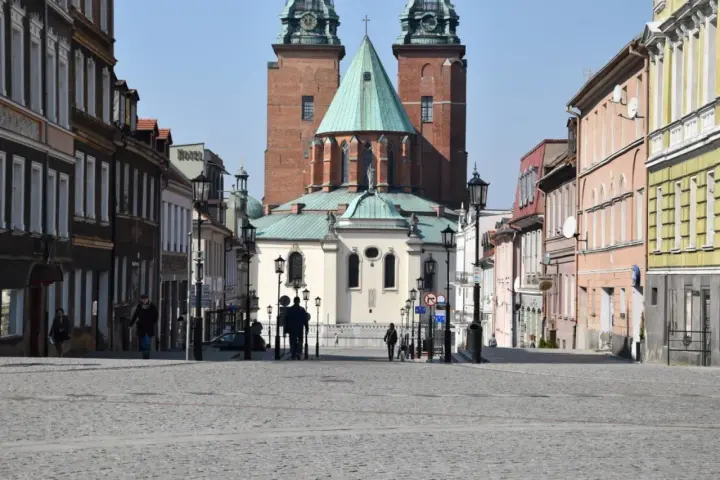 Spacer po brukowanym rynku Gniezna, z katedrą w tle. Kolorowe kamienice po bokach tworzą urokliwą atmosferę.