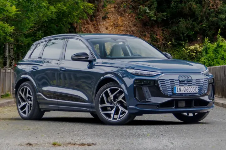 Elegancki, ciemnoniebieski Audi Q6 e-tron stoi na tle zieleni.