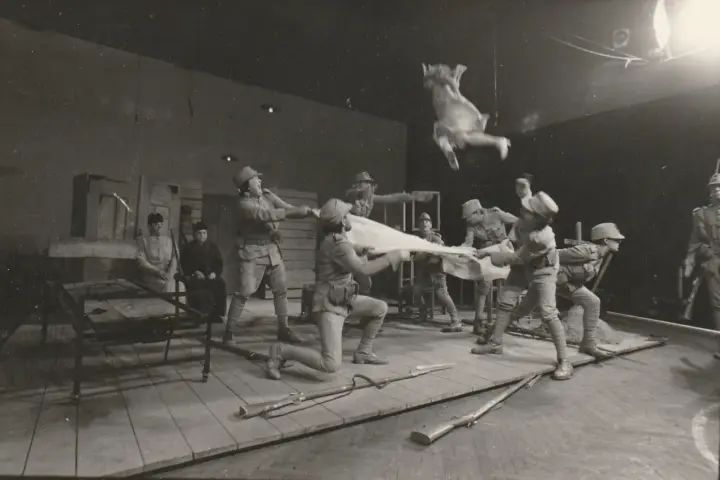 Scena teatralna: żołnierze w mundurach z epoki, jeden w powietrzu, trzymają białą tkaninę. Kantor Wielopole.