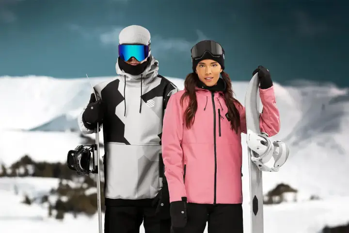 Pareja con tablas de snowboard, ella con chaqueta rosa, él con chaqueta gris y negra. Opiniones sobre Sorona Aura: ¡calidez y estilo en la montaña!