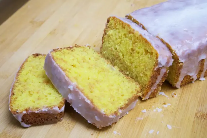Un delicioso pastel de limón, cubierto con glaseado blanco, cortado en rebanadas sobre una tabla de madera.