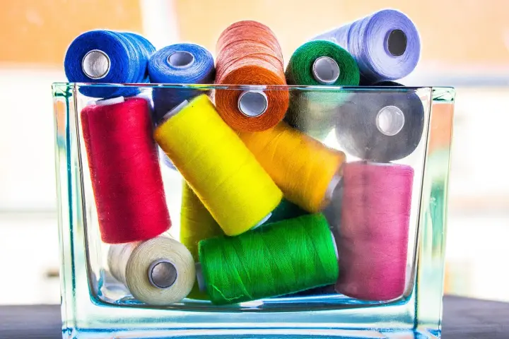 Un assortiment coloré de bobines de fil coton ou polyester, empilées dans un pot en verre.