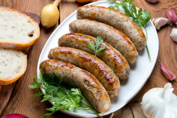 Pięć soczystych białych kiełbasek z piekarnika, podanych z chlebem, cebulą i czosnkiem.