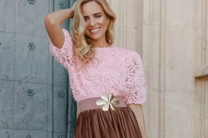 Mujer sonriente con top rosa de encaje y falda marrón, ideal para una boda en octubre, manga corta o larga.