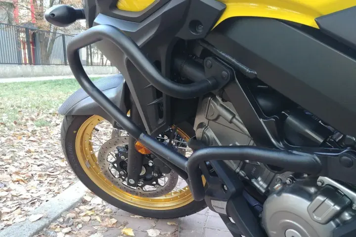 Żółty motocykl z czarnymi gmolami chroniącymi silnik i osłony. Złota obręcz koła i tarcza hamulcowa.