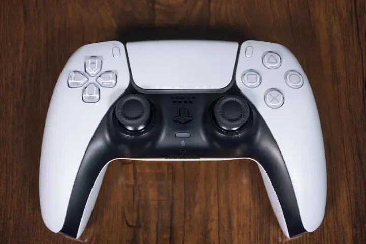 Biały kontroler DualSense do PS5 leży na drewnianym blacie. Zastanawiasz się nad ps4 pobór prądu?