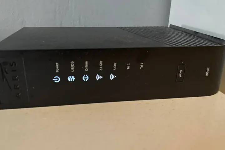 Czarny router Arris TG2492 z widocznym przyciskiem WPS i wskaźnikami stanu: Power, US/DS, Online, 2.4 GHz, 5 GHz, Tel 1, Tel 2.