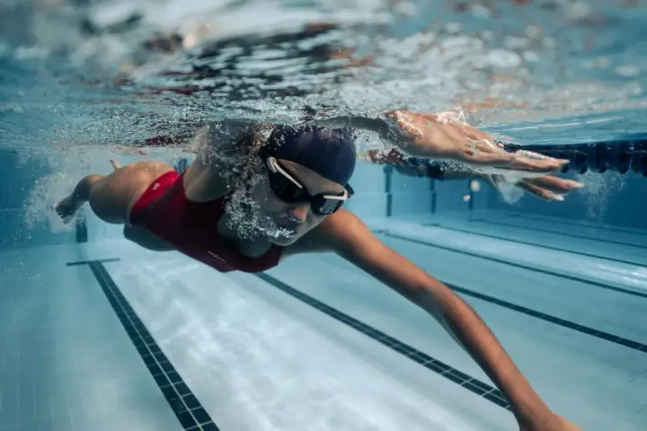 Une femme en maillot de bain rouge nage en crawl, lunettes de natation sur le nez. Sa **natation transformation physique femme** est visible sous l'eau.