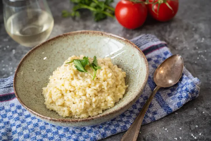 Cremiges Risotto, perfekt als Grundrezept für viele Variationen. Mit frischer Petersilie garniert, daneben ein Glas Weißwein und Tomaten.