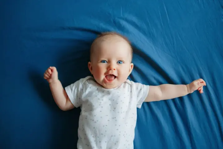 Un bimbo sorridente, con occhi azzurri e braccia aperte, celebra il suo scatto di crescita di 4 mesi su un telo blu.