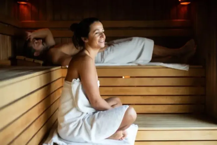 Para relaksu w saunie. Kobieta w ciąży i mężczyzna odpoczywają w drewnianej saunie, otuleni ręcznikami.