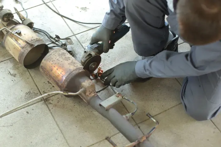 Meccanico con smerigliatrice effettua la rimozione fap da un pezzo di scarico auto, scintille volano.
