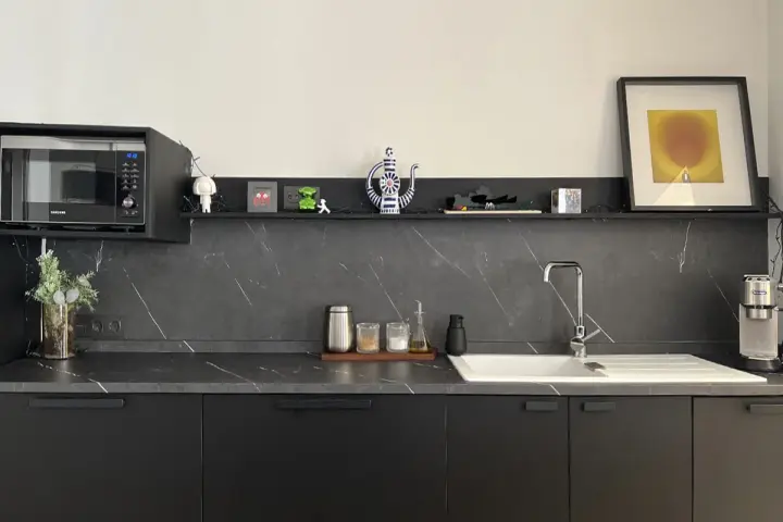 Encimera de cocina negra con vetas blancas, lista para cambiar. Microondas, fregadero y decoración moderna.