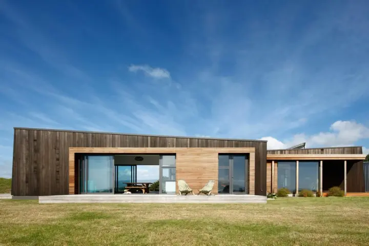 Maison moderne en bois avec grande baie vitrée, deux chaises invitantes sur la terrasse. Une extension maison container stylée.