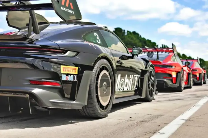 Czarny Porsche GT3 RS z numerem 3 i logo Manthey na skrzydle, gotowy do wyścigu obok czerwonych samochodów.
