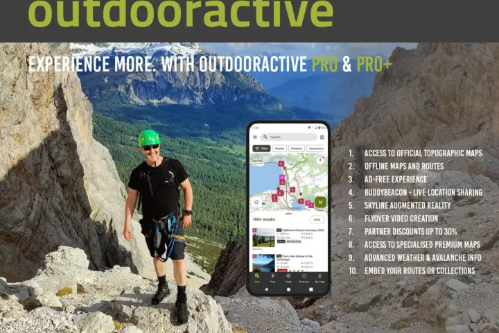 Escursionista sorridente in montagna, con smartphone che mostra l'app outdooractive gratis con mappe e percorsi.