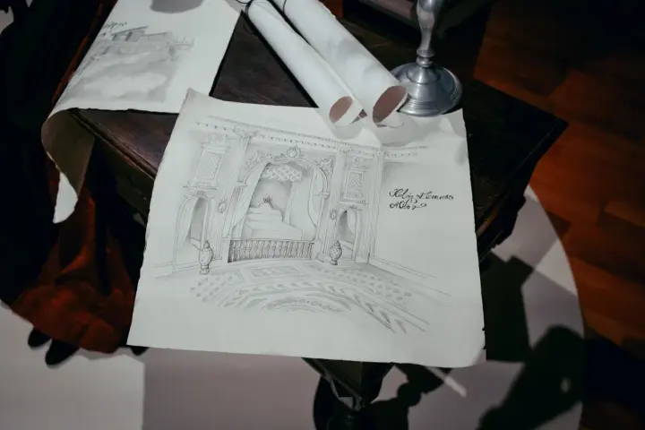 Szkice architektoniczne wnętrza, jakby z lekcji korepetycje z rysunku. Widać łóżko z baldachimem, balustradę i zdobioną podłogę.